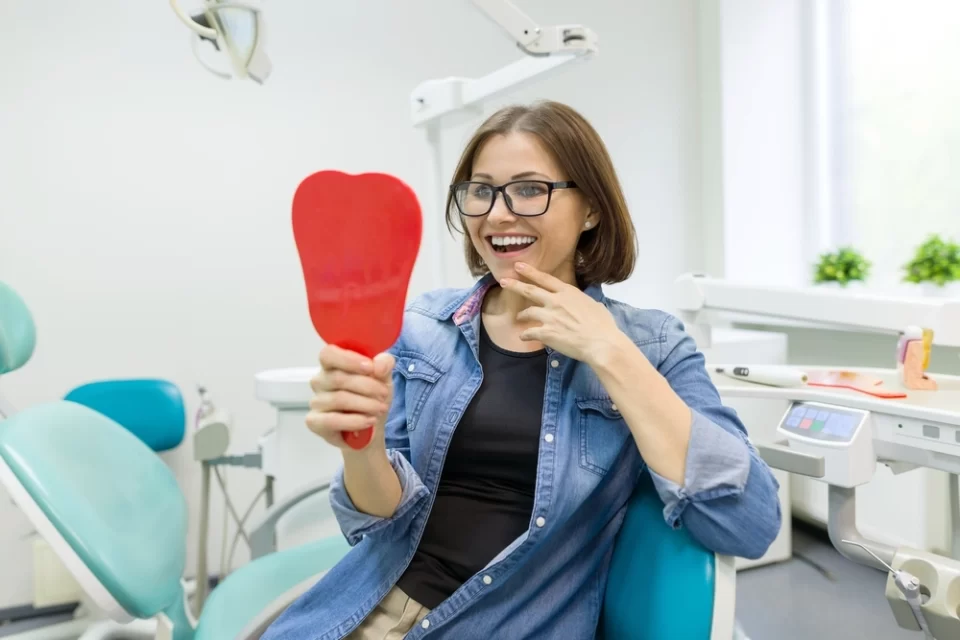smiling woman sitting in dentist chair and looking into a mirror in Sumter, SC