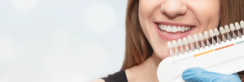 woman smiling and holding a sleeve of false teeth in different shades | Restorative Dentistry | fillings