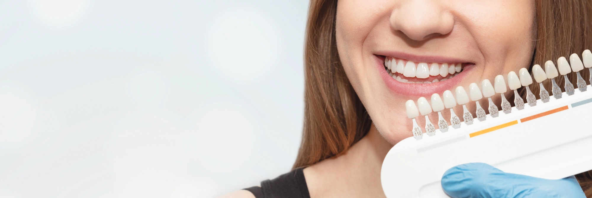 woman smiling and holding a sleeve of false teeth in different shades | Restorative Dentistry | fillings
