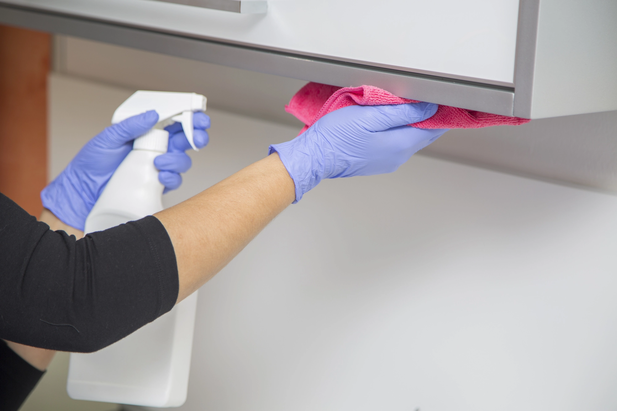 close up of woman with spray bottle and cloth cleaning under a dentist office cabinet