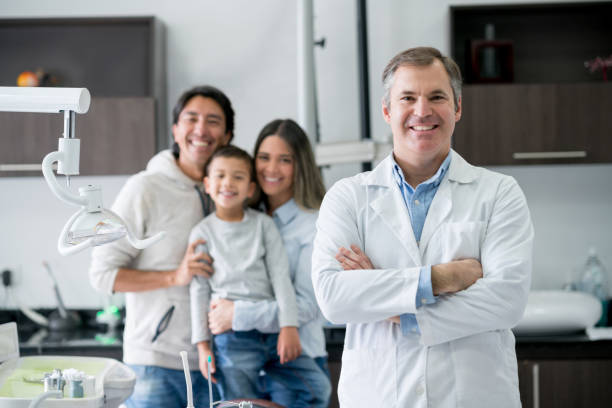 Portrait of a dentist at the office looking very happy with a family at the background and smiling - healthcare and medicine concepts